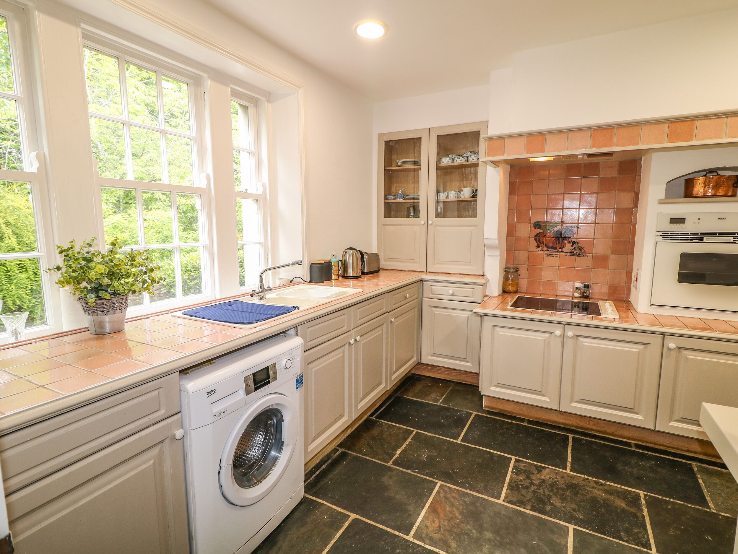 A kitchen with a washing machine, a sink, cabinets, and a tiled backsplash.
