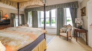 A bedroom with a four-poster bed, a sitting area with a chair, a desk, and a television on a dresser. - Scarvagh House (Craigavon)