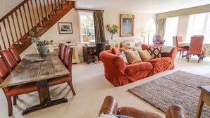 A spacious living room with a wooden staircase, a dining area with a wooden table and chairs, a red sofa set, and a large window with curtains. - Scarvagh House (Craigavon)