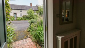 A view through a window into a courtyard with a brick pathway, a house with a green door, and a mirror on the wall. - Scarvagh House (Craigavon)