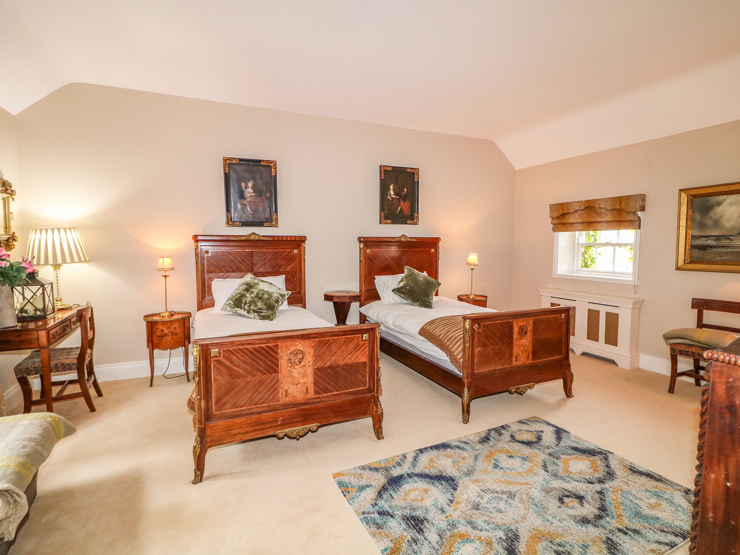 A bedroom with two wooden beds, a sitting area with a chair, a small table, and a lamp.