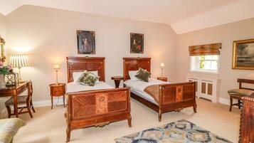 A bedroom with two wooden beds, a sitting area with a chair, a small table, and a lamp.