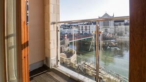 Une vue depuis un balcon doté d’une balustrade en verre, donnant sur un canal, des bâtiments et un pont.