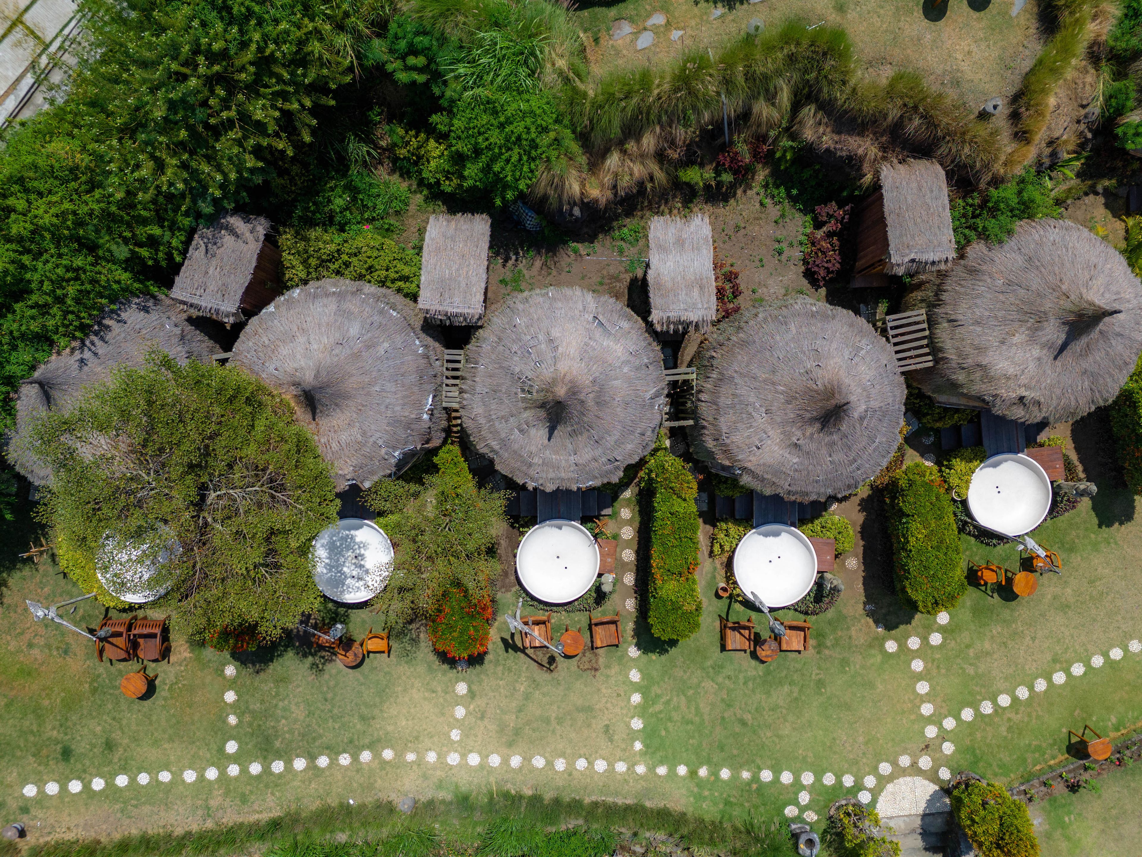 An aerial view of a resort with thatched-roof structures, outdoor seating, and circular water tanks.