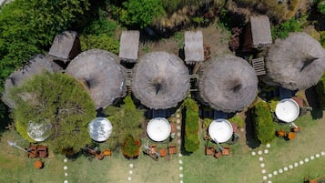 An aerial view of a resort with thatched-roof structures, outdoor seating, and circular water tanks.