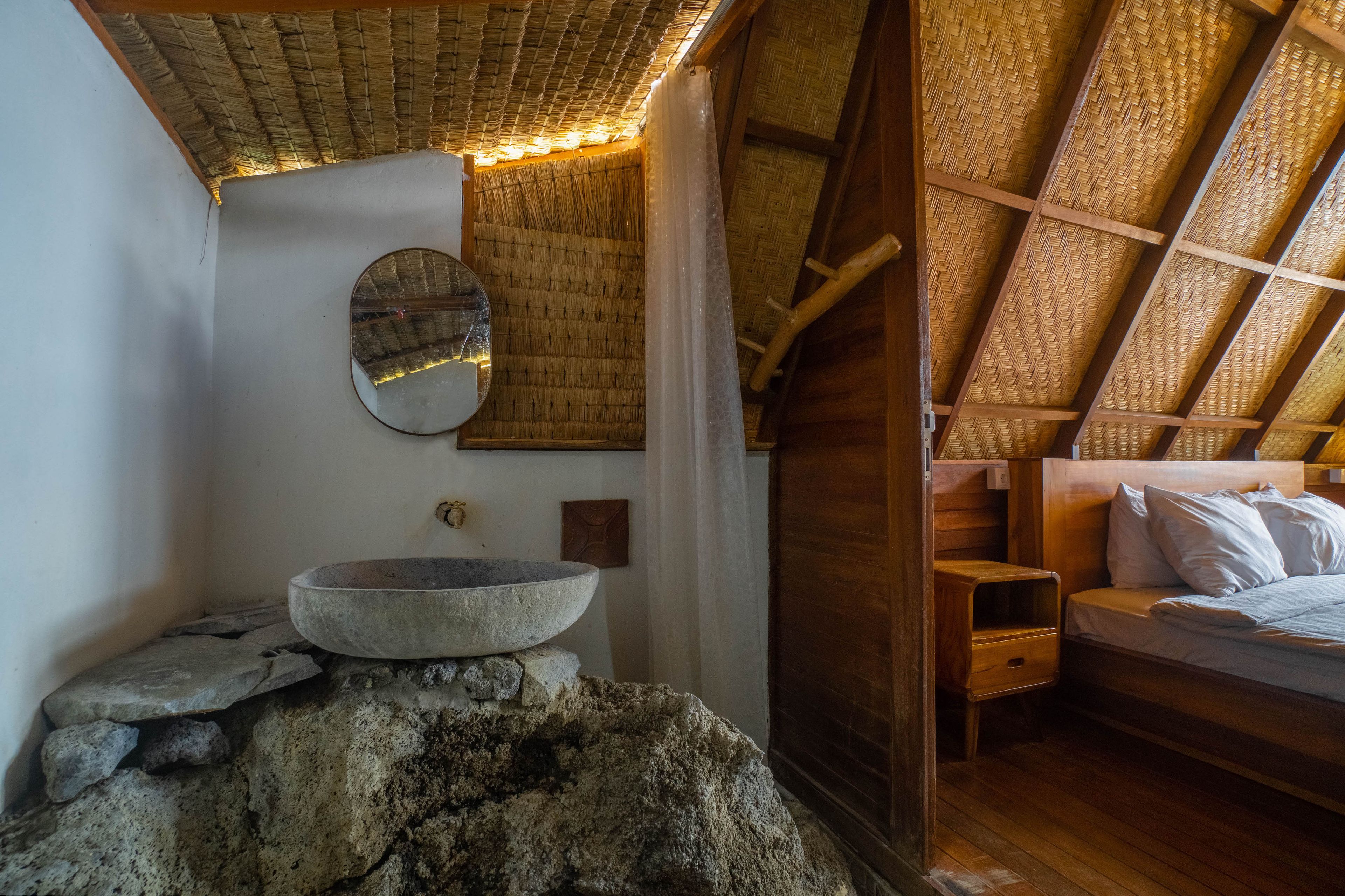 A rustic room with a stone basin, wooden bed, and a woven ceiling.