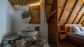 A rustic room with a stone basin, wooden bed, and a woven ceiling.