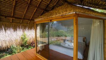 A room with a glass enclosure, wooden flooring, and a thatched roof.