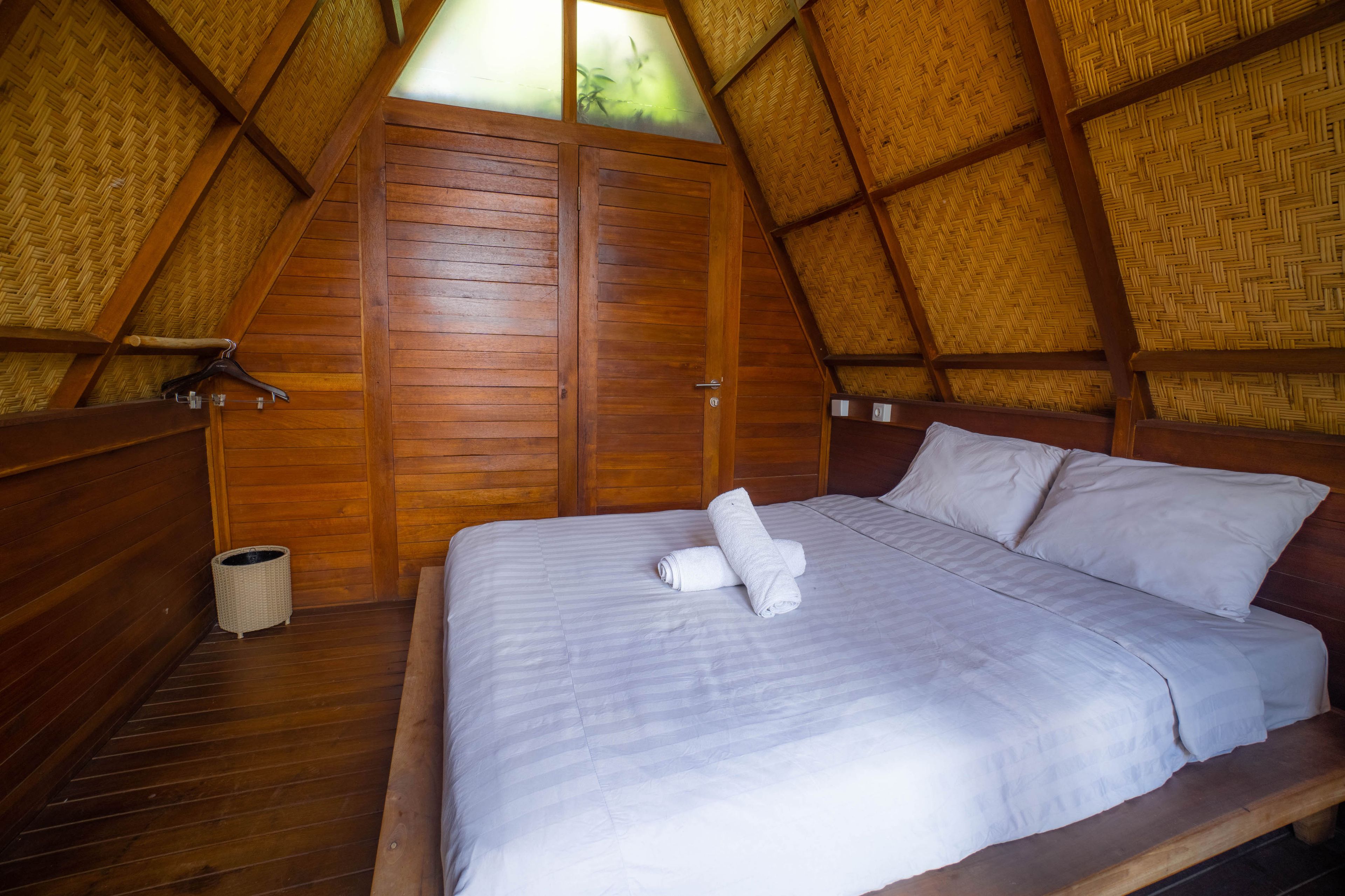 A single bed with a white mattress and pillows, a wooden headboard, and a woven ceiling.