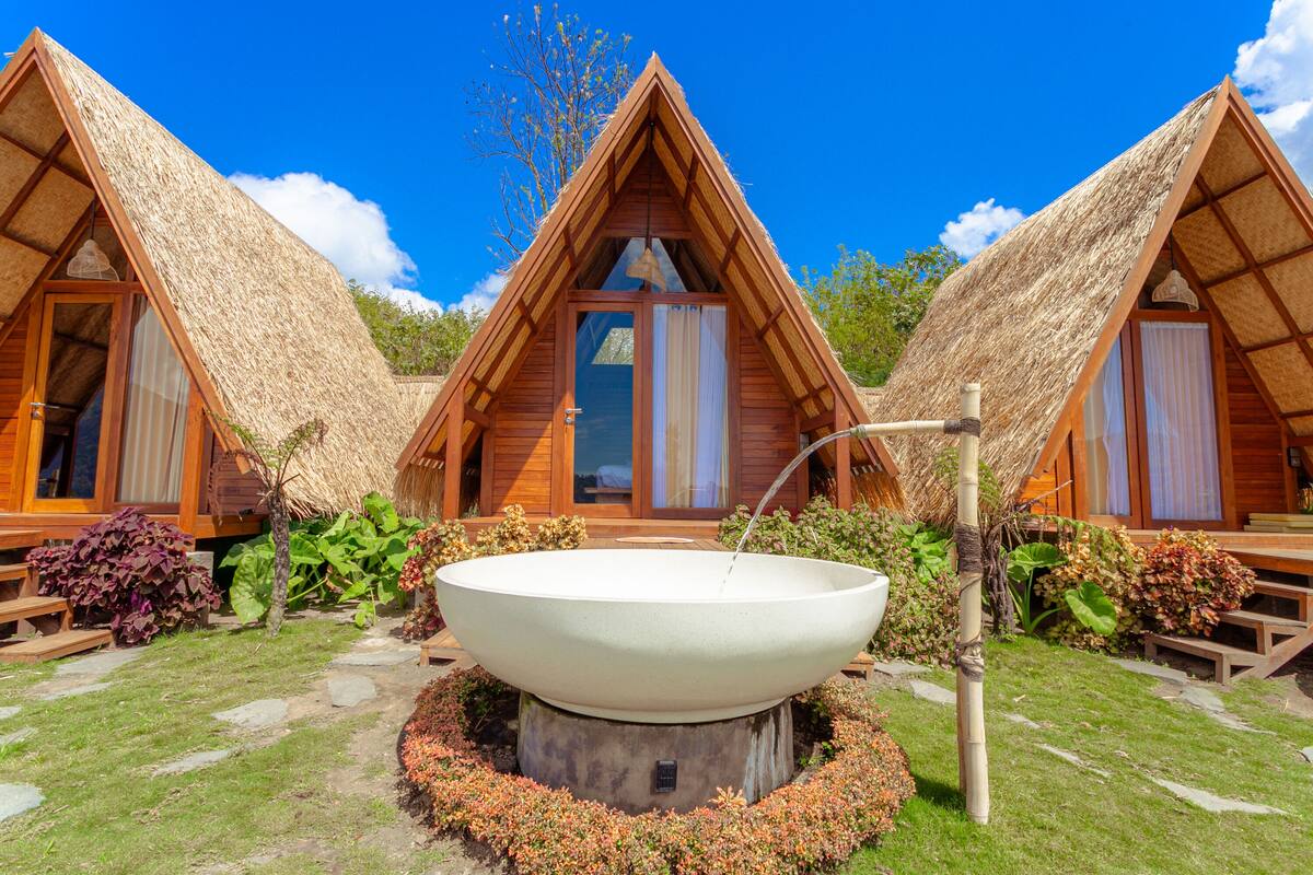 A bungalow-style hotel with thatched roofs, a central water feature, and a garden with various plants.