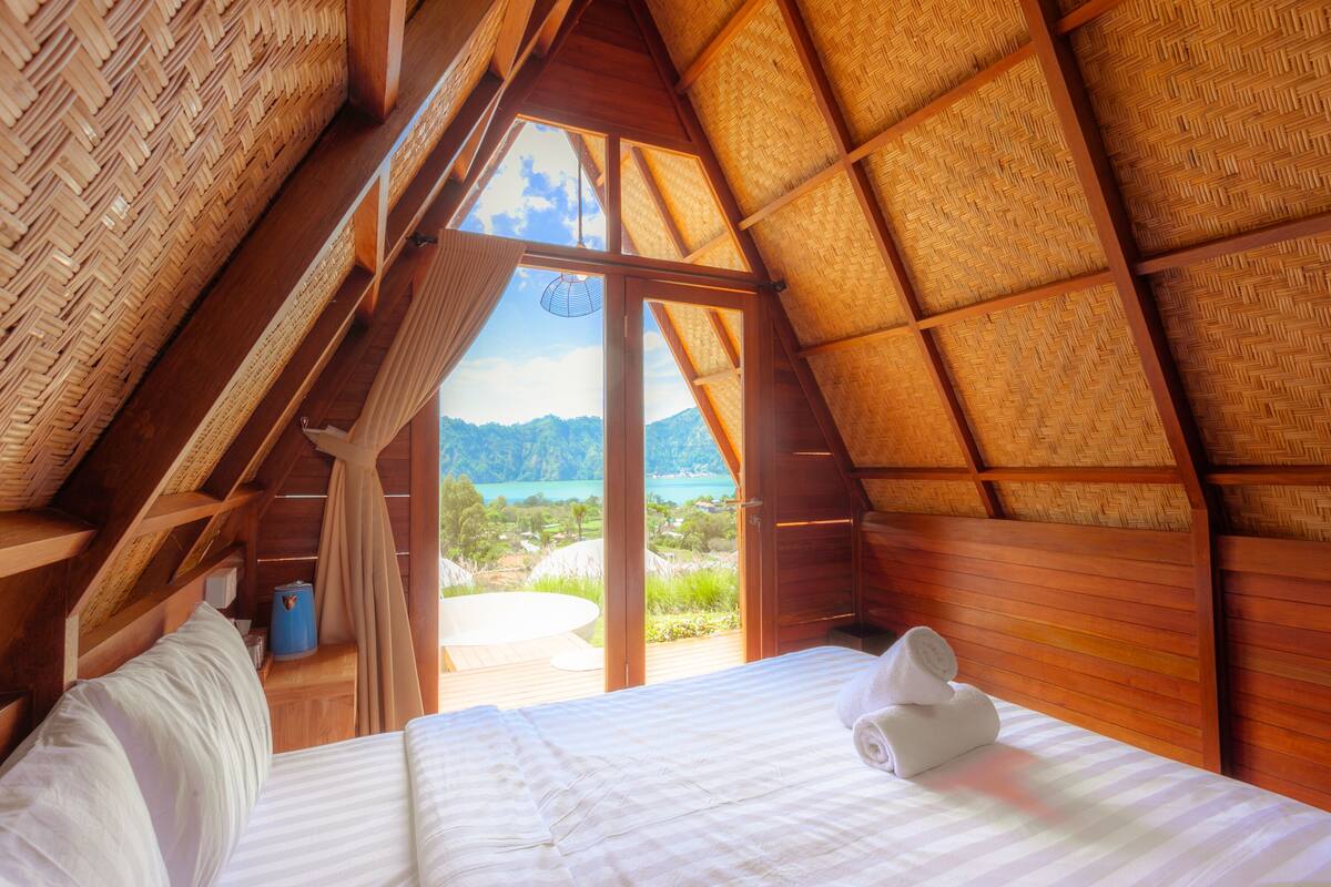 A bedroom with a wooden ceiling and a large window overlooking a scenic landscape.