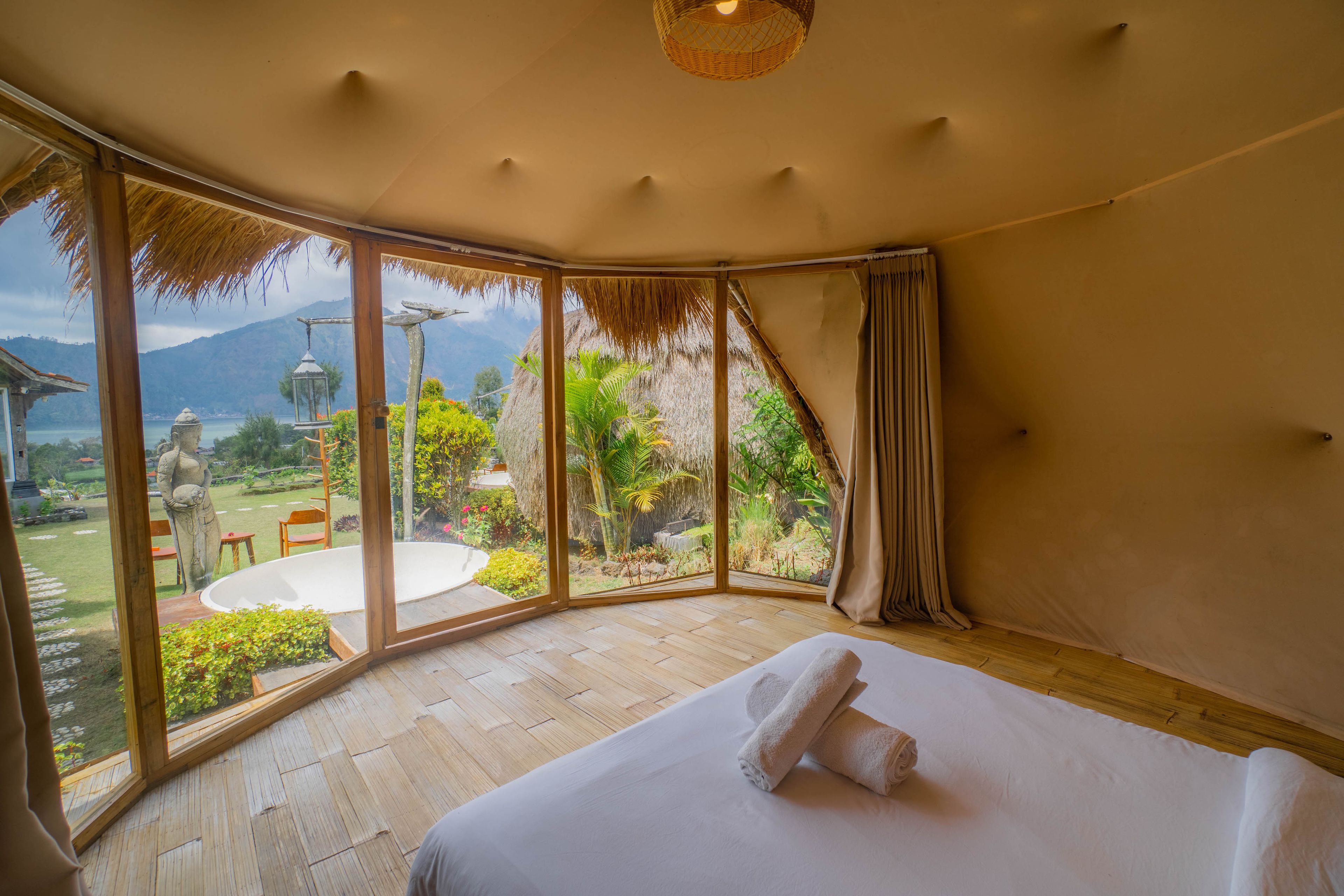 A room with a large bed, a view of a garden, and a statue outside.