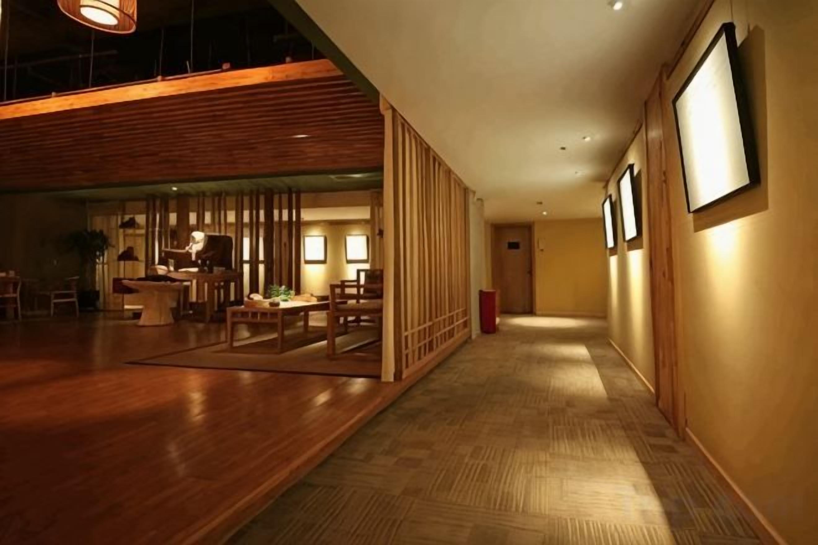 A hotel corridor with wooden flooring, a seating area with tables and chairs, and framed pictures on the walls.