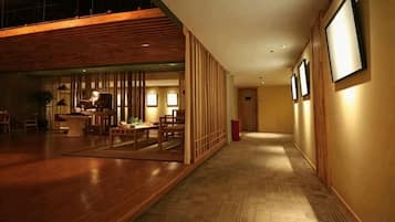 A hotel corridor with wooden flooring, a seating area with tables and chairs, and framed pictures on the walls.