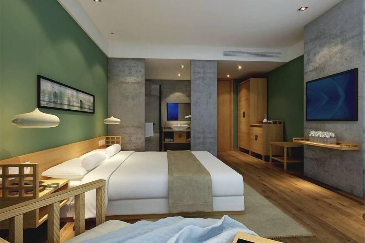 A modern hotel room with a large bed, a desk, a chair, a TV, and a bathroom visible in the background.