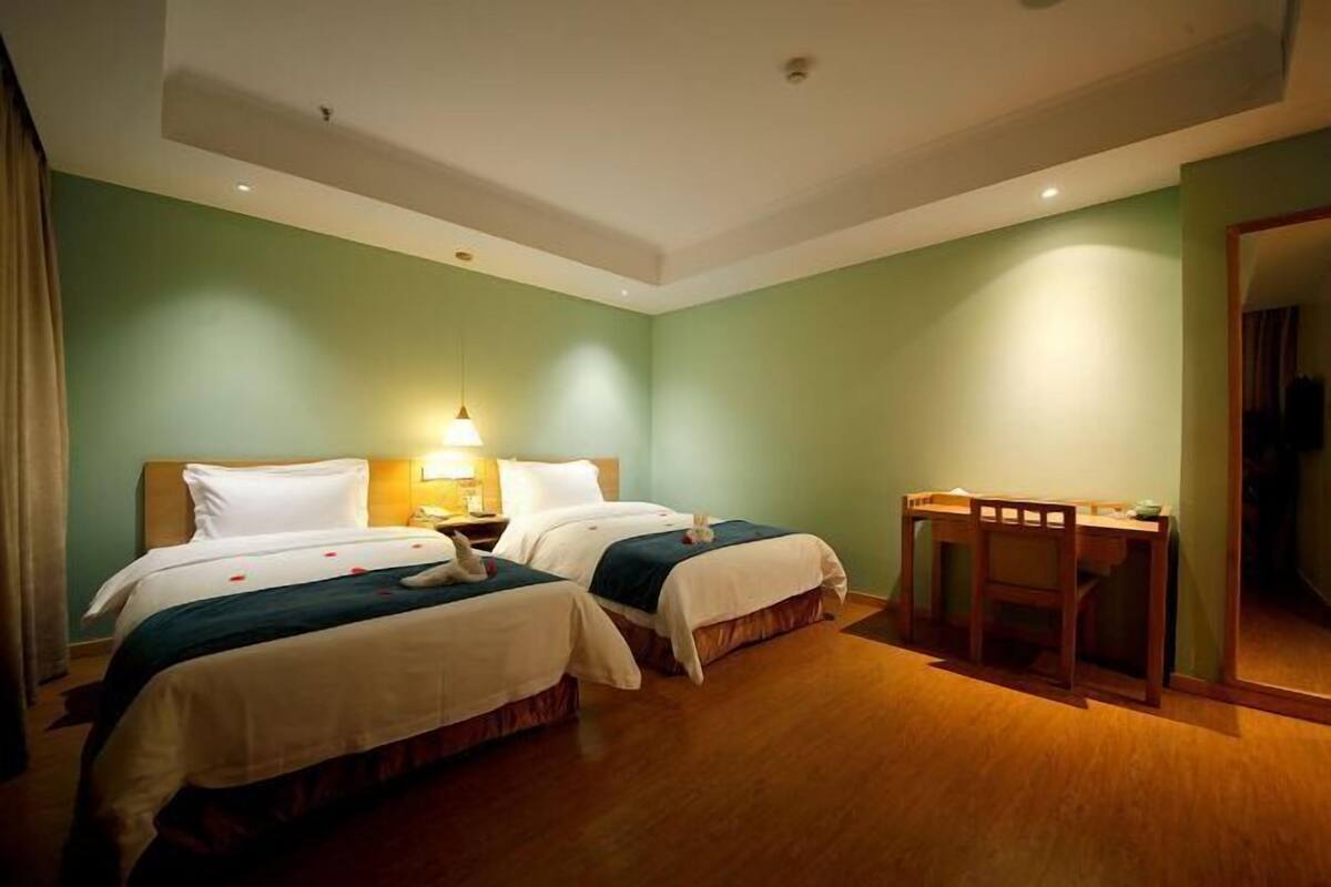 A hotel room with two beds, a desk, and a mirror.