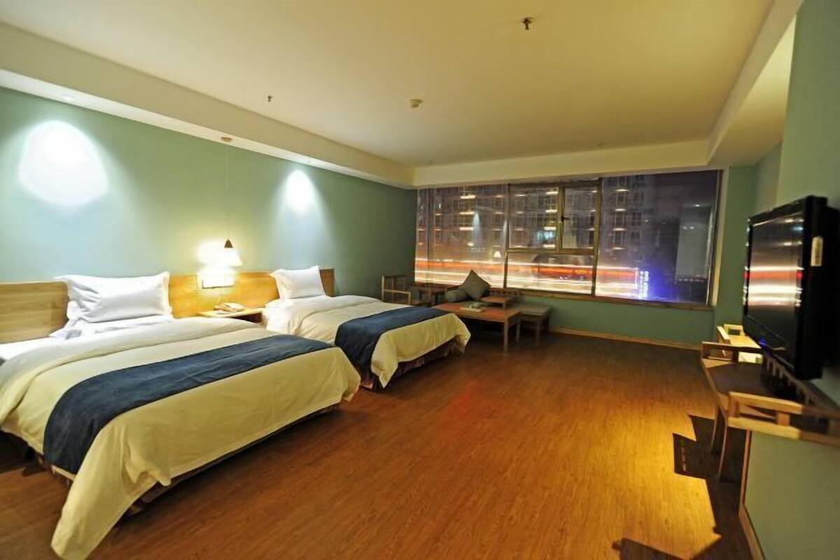 A hotel room with two beds, a desk, a chair, a TV, and a large window with a city view.