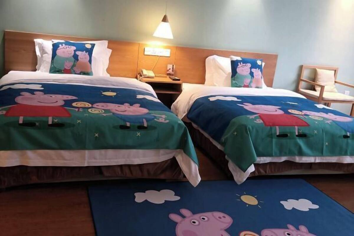 A hotel room with two beds, each with a cartoon-themed bedspread, a bedside table with a lamp, and a chair.