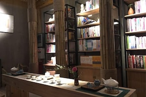 A library with bookshelves, a long table with teapots, and a vase with flowers. - NengHui Star Hotel (Guiyang)