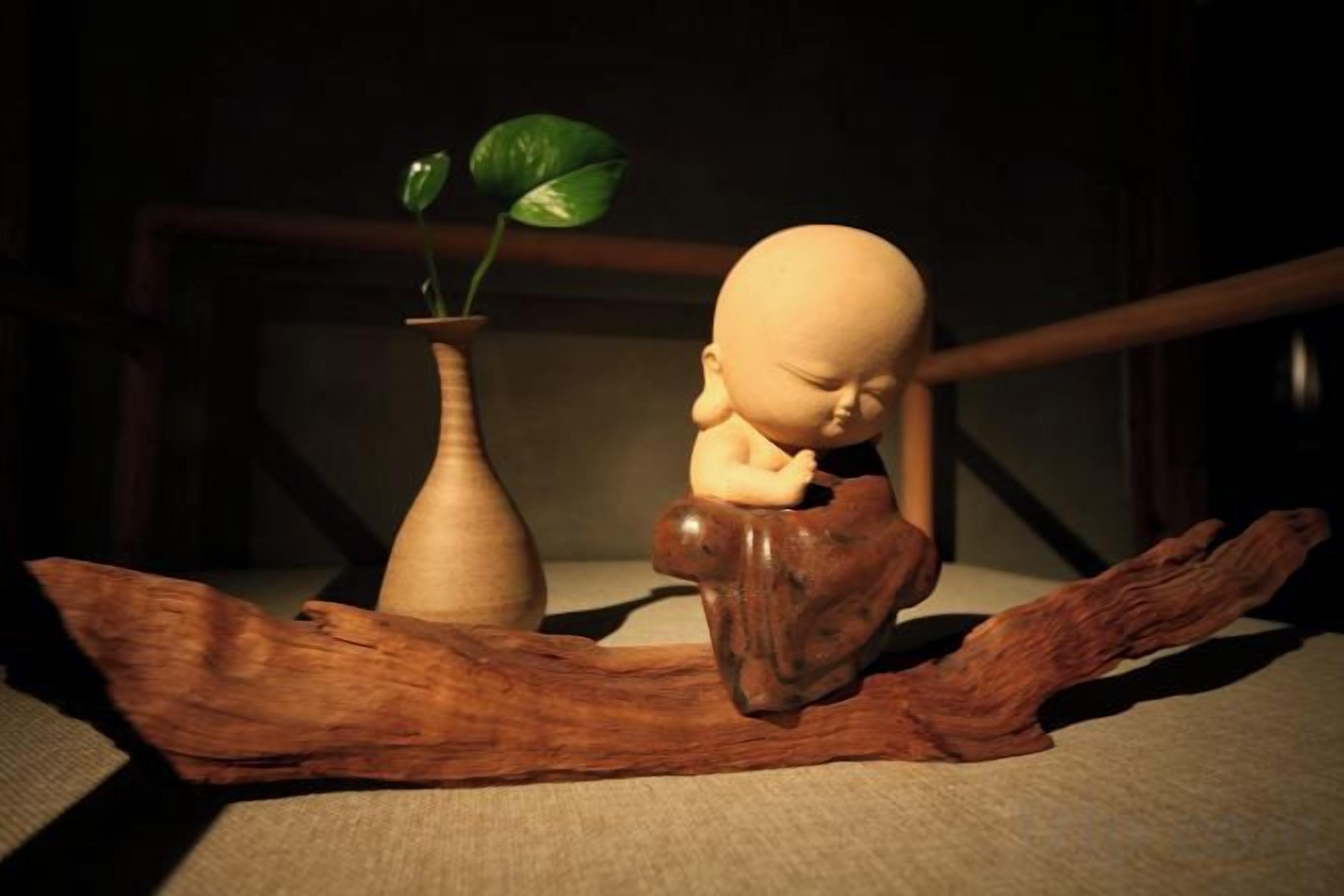 Une sculpture en bois représentant un bébé, posée sur une branche, avec un vase et une plante.