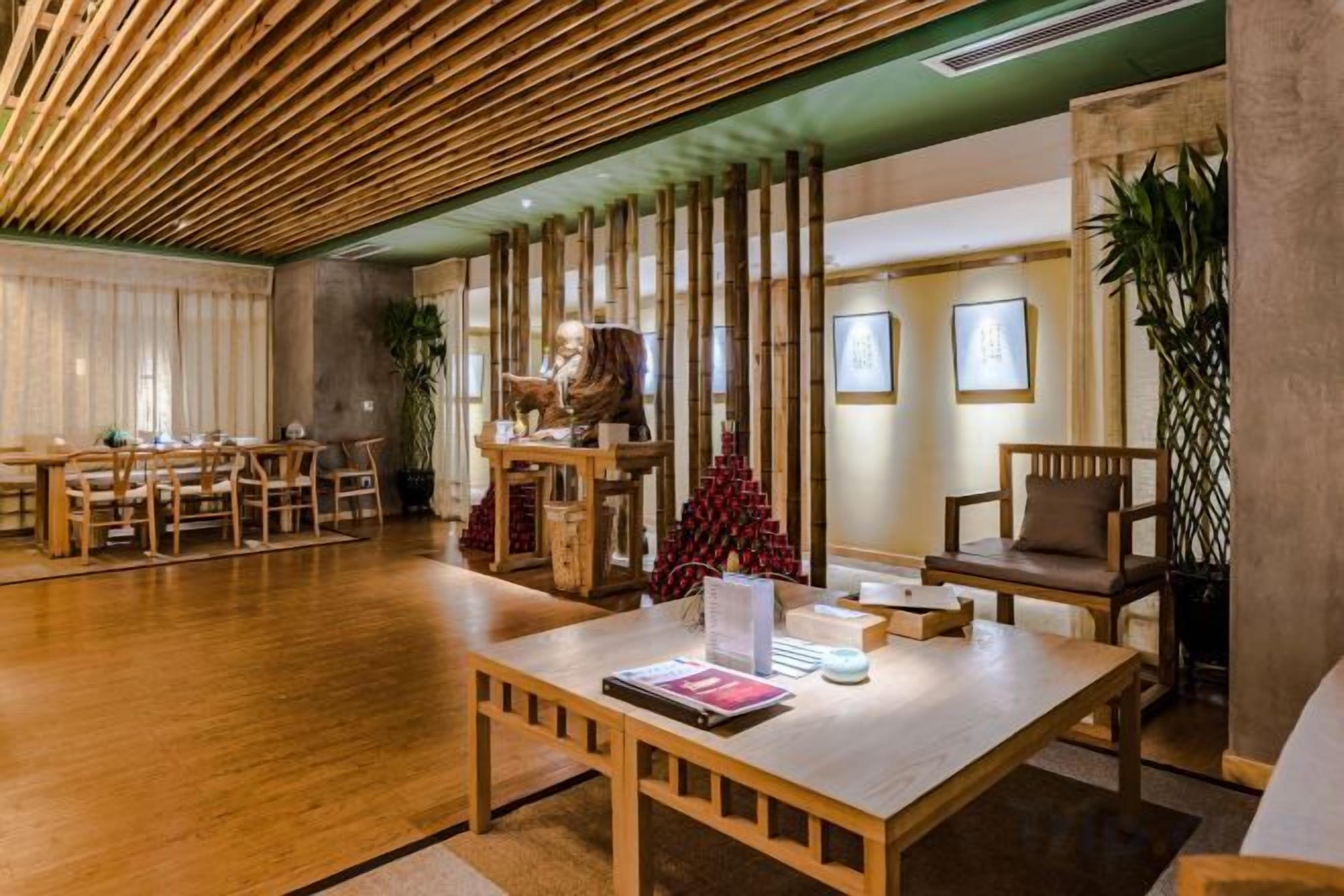 Vestíbulo de hotel con techo de madera, mostrador de recepción, zona de estar y una planta grande.
