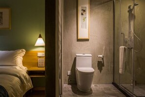 A hotel bathroom with a toilet, a shower, and a bed in the adjacent room. - NengHui Star Hotel (Guiyang)
