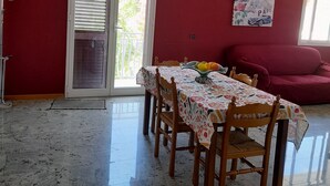 Uma área de refeições com uma mesa posta para quatro pessoas, um sofá vermelho e uma porta que dá para uma varanda.
