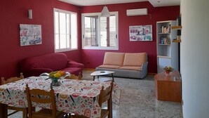 Uma sala ampla com uma mesa de jantar, sofás vermelhos e uma estante de livros.