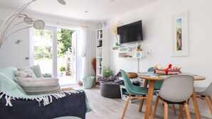Una sala de estar moderna con un sofá, una mesa de comedor con sillas, un televisor montado en la pared y una estantería.