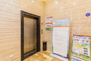 An elevator in a hotel lobby with marble walls, a trash bin, and informational posters. - Yasidun Hotel (Hohhot Convention and Exhibition Center) (Hohhot)