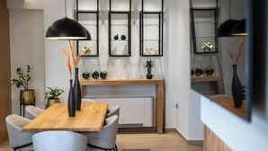 Een moderne eetruimte met een houten tafel en stoelen, een zwarte hanglamp en decoratieve objecten op planken.