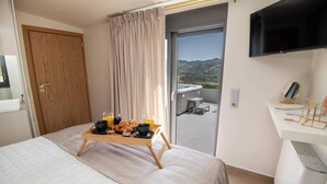 Een hotelkamer met een bed, een ontbijtplateau, een televisie en een balkon met uitzicht op de bergen.