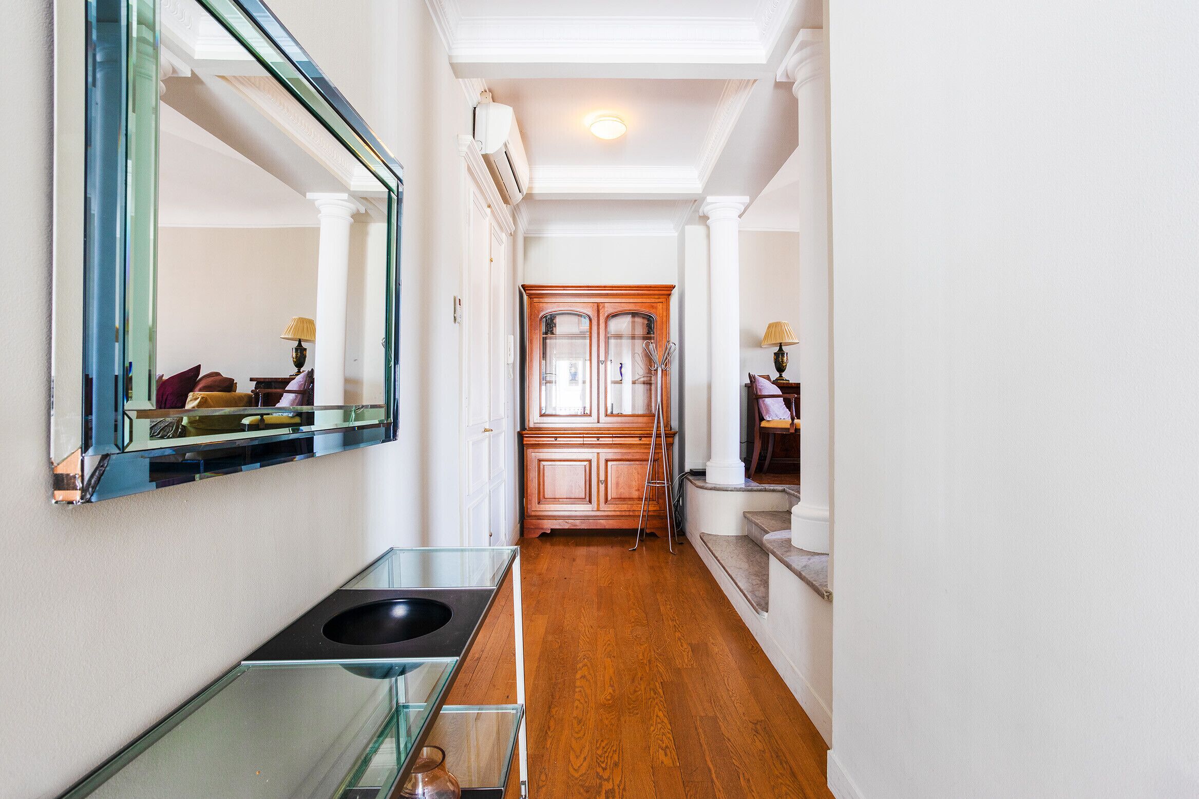 A hallway with a wooden floor, a glass sink, and a wooden cabinet.