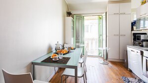 Cozinha compacta com armários brancos, micro-ondas e um pequeno espaço de refeições com mesa de vidro e cadeiras.