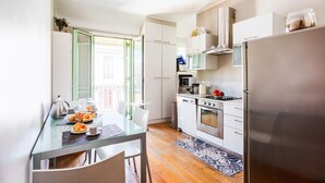 Cozinha moderna com armários brancos, geladeira de aço inoxidável e área de jantar com mesa e cadeiras de vidro.