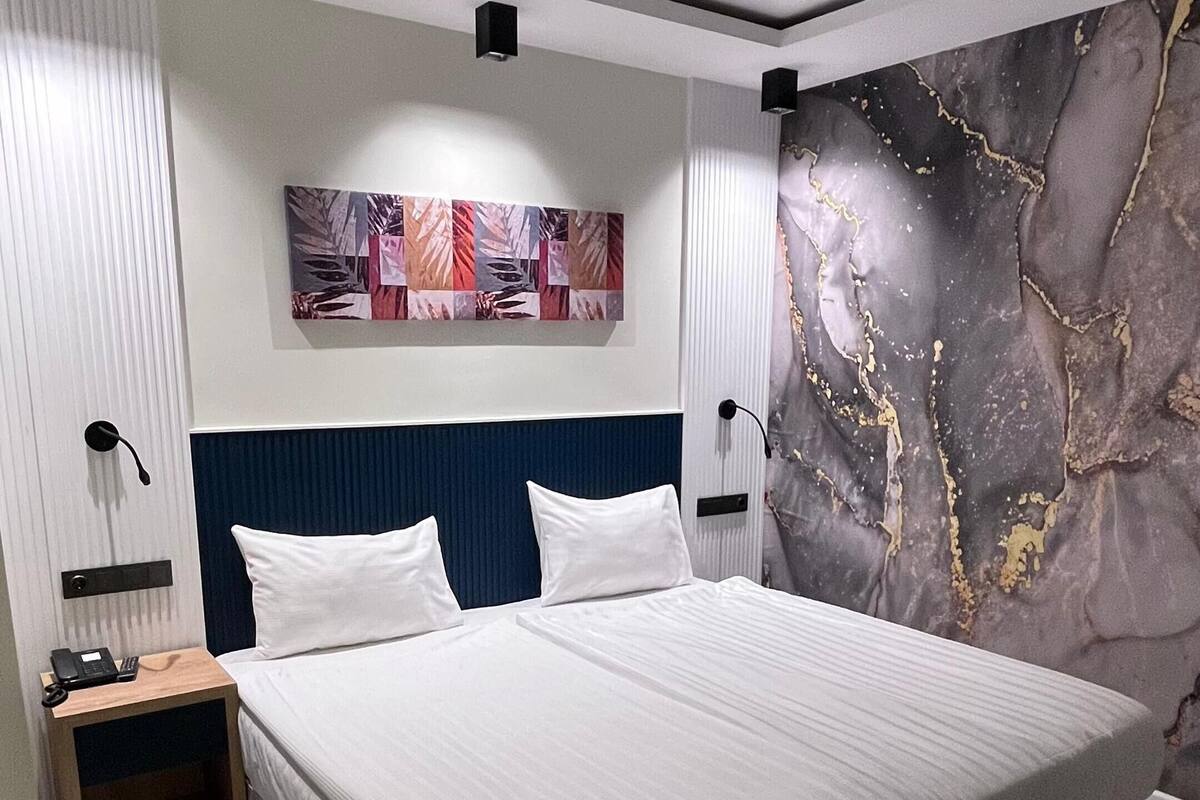 A modern bedroom with a large bed, a headboard, a bedside table with a phone, and a wall with a marble-like design.