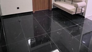 Quarto moderno com piso de mármore preto, porta de madeira com uma placa e sofá bege.