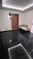 Una habitación moderna con suelo de mármol negro, una puerta de madera con un letrero y un sofá beige.