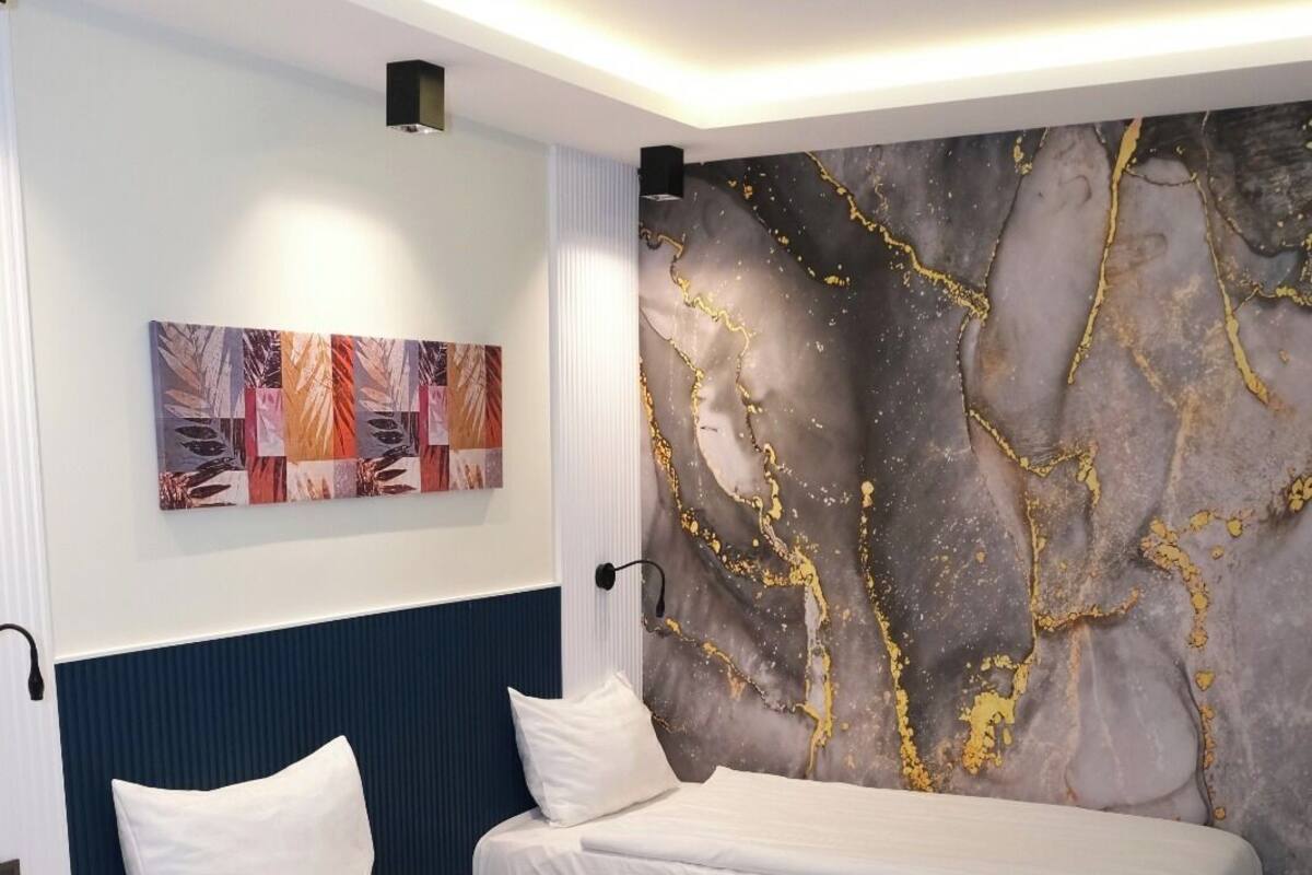 A modern hotel room with two beds, a marble accent wall, and a small side table.