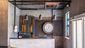 Uma área de recepção com relógio, luminárias pendentes e design moderno, com parede de pedra e detalhes em metal.