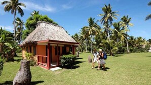 A thatched-roof hut with a wooden porch, surrounded by palm trees and a grassy area. - Nabua Lodge Hidden Getaway (Nacula Island)