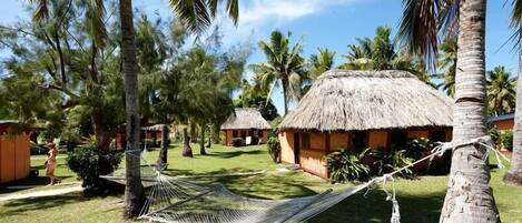Un resort tropical con cabañas de techo de paja, palmeras y una hamaca.