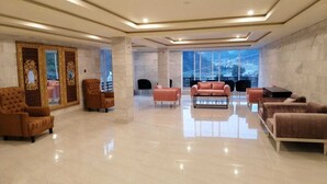 Un vestíbulo amplio con techo alto, ventanas grandes y una variedad de opciones de asiento, incluyendo sofás y sillones.