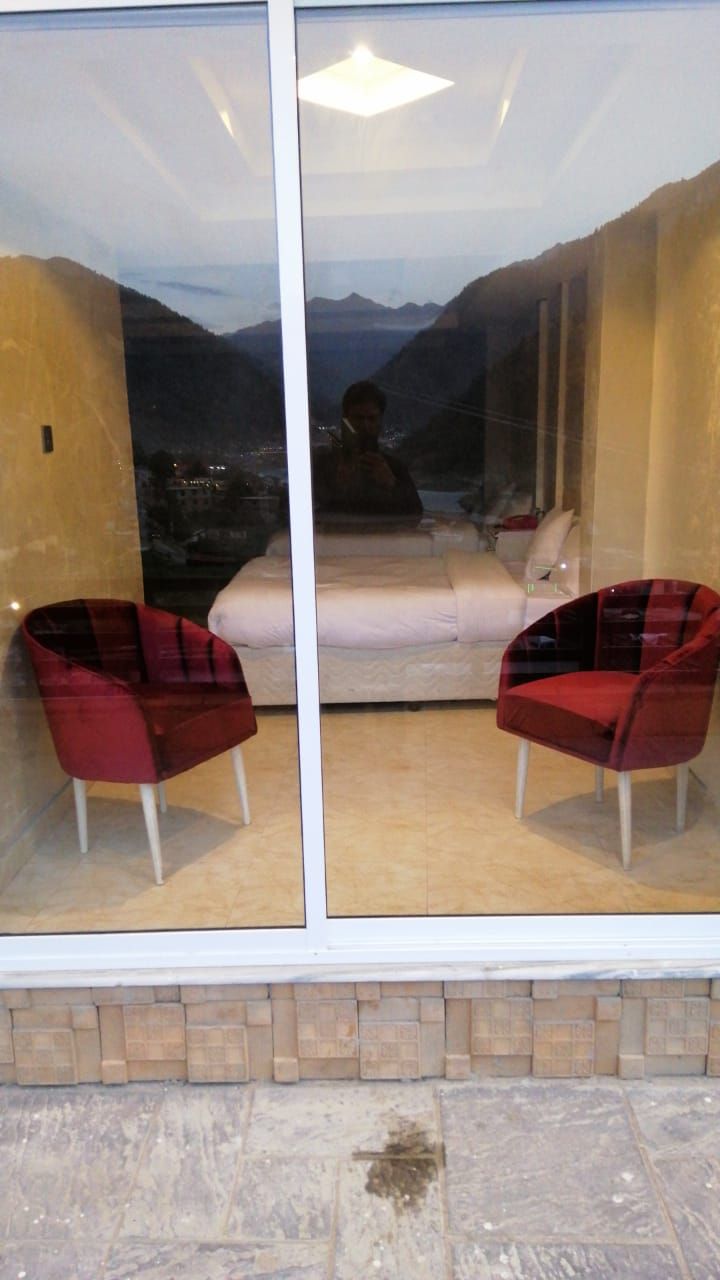 A room with a large window offering a view of mountains and a lake. There are two red chairs and a white sofa.