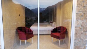 Una habitación con una cama, dos sillas rojas y vistas a las montañas a través de un muro de cristal.