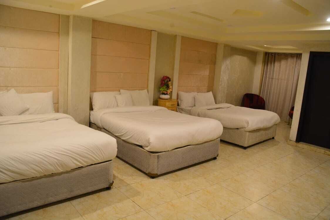 A hotel room with three beds arranged in a row, a small table with a vase of flowers, and a chair.