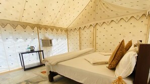 A tented room with a bed, a small table with a lamp, and a decorative lantern. - Barna Desert Camp (Jaisalmer)