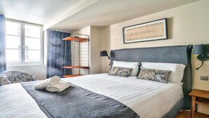 Ein Hotelzimmer mit einem großen Bett, einem Nachttisch, einem Sessel, einem Fenster mit Vorhängen und einer Wandlampe.