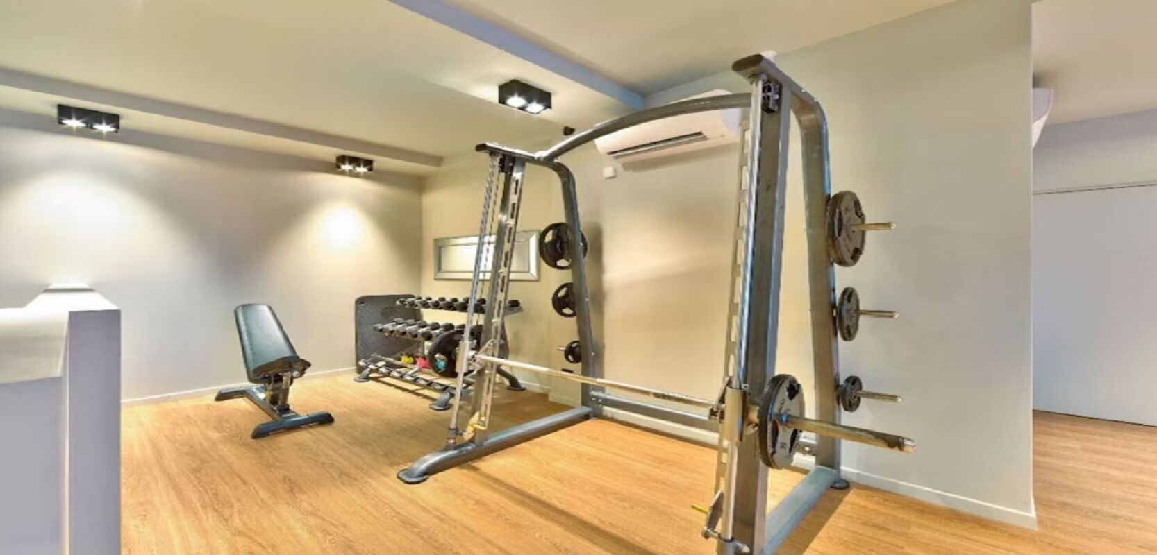 A modern gym with a squat rack, bench press, and various weight plates.