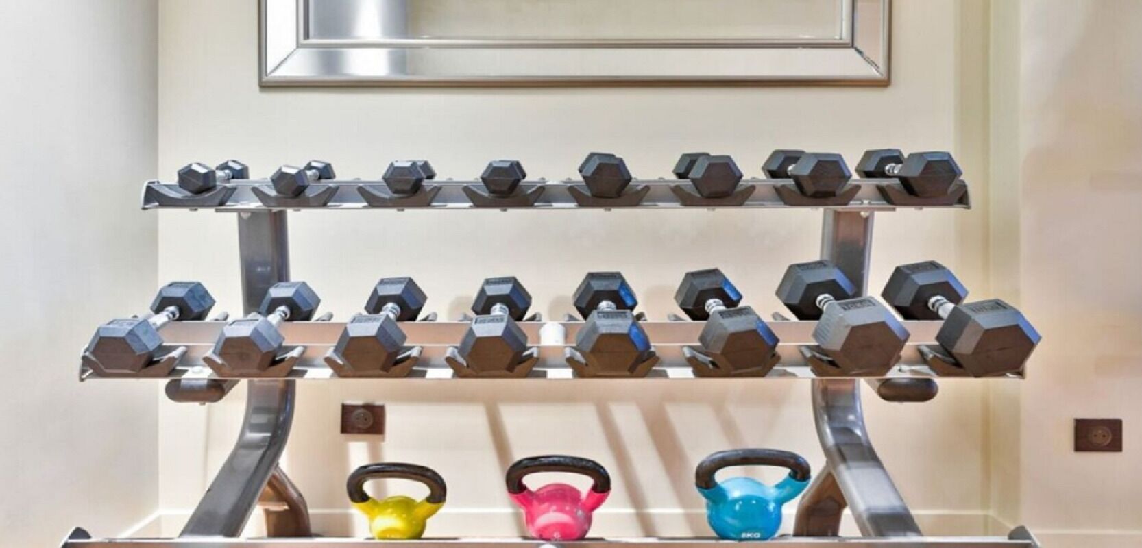 Et vægmonteret vægtstativ med flere sæt håndvægte og kettlebells.